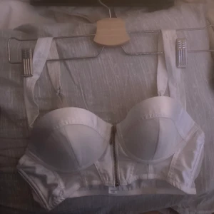 Vit bustier - En mycket fin vit bustier i storlek 75A. Själva toppen skulle jag säga passar XS-S eventuellt en liten M.  Bustiern är i sig i bra skick och inte nopprig alls. Betalning sker via swish och fraktar spårbart som kostar 66kr! Hör av er vid funderingar eller vid intressen! 