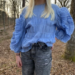 Blå blus  - En blå blus som inte är använd. Bra skick. Volanger på armarna. Inte genomskinlig men hyfsat tun