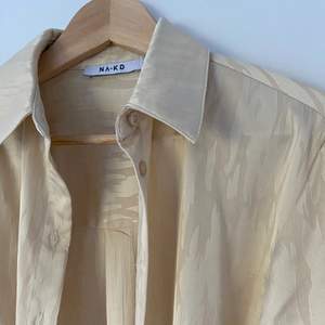 En oversize silkig skjorta i en ljus beige färg, har ett svagt mönster på sig. Använd fåtal gånger så gott som ny. Storlek 32 men sitter som en 36/38