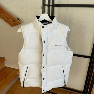 Vit puffer väst - Säljer nu min favorit väst då jag tyvärr behöver rensa ut bland alla mina jackor! Västen är i tjockt material och man känner på den att den är av kvalite! Den är köpt från ett märke som heter rockport! Västen är i så bra skick den kan vara med tanke på att den är köpt second hand tidigare med! Den är i strl XS men sitter som en större S🥰