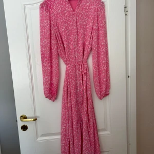 Rosa blommig klänning från MSCH Copenhagen - Säljer en superfin rosa långklänning från MSCH Copenhagen. Den har ett blommigt mönster och långa ärmar. Klänningen är i nyskick och har ett knytband i midjan för en smickrande passform. Perfekt för vår och sommar!