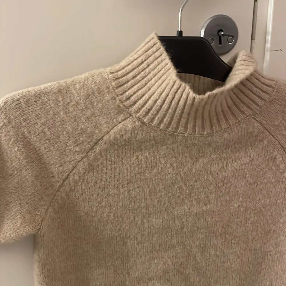 Beige stickad kort ärmad med polo, knappt andvänd och väldigt tretshigt material. Stickat.