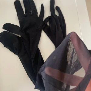 Svarta eleganta handskar - Säljer ett par svarta eleganta handskar i tunt material. Perfekta för en stilren look. De är långa och ger en sofistikerad touch till vilken outfit som helst. Passar bra för speciella tillfällen eller som en chic accessoar.