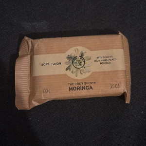 Moringa tvål från The Body Shop - En härlig tvål från The Body Shop med moringa fröolja. Tvålen väger 100 g (3.5 oz) och är perfekt för att ge huden en mjuk och fräsch känsla. Förpackningen är enkel och naturlig, vilket speglar produktens rena ingredienser.