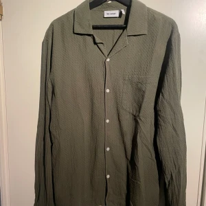Olivgrön skjorta från Weekday - Snygg olivgrön skjorta från Weekday med en texturerad yta och klassisk krage. Skjortan har långa ärmar och knappar framtill. Perfekt för en stilren look. Har två mindre syndliga fläckar, se bild, kan gå bort i tvätten!! Är storlek S men passar även M beroende hur man vill att den ska sitta! På mig satt den som en M. Hör av dig vid frågor!