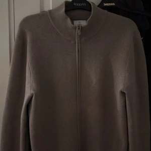 Beige kofta från Bläck - Snygg beige kofta från Bläck med dragkedja framtill. Perfekt för lager-på-lager under kyliga dagar. Den har en ribbad krage och är tillverkad i ett mjukt material för extra komfort.