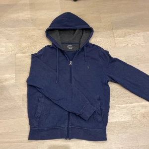 Mörkblå hoodie från Ralph Lauren - Säljer en snygg mörkblå zip hoodie från Ralph Lauren. Den har en dragkedja framtill och en justerbar huva. Perfekt för en avslappnad stil.