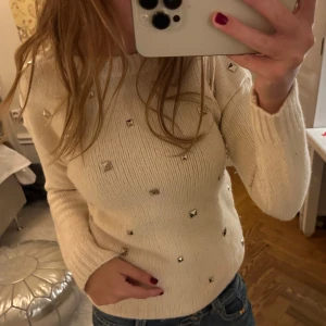 Vit stickad tröja med nitar - Säljer en snygg vit stickad tröja dekorerad med nitar. Tröjan har långa ärmar och en rund halsringning.