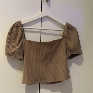 Beige ribbad topp - Snygg beige ribbad topp med puffiga korta ärmar. Perfekt för en stilren look. Toppen har en fyrkantig halsringning och är croppad för en modern touch.