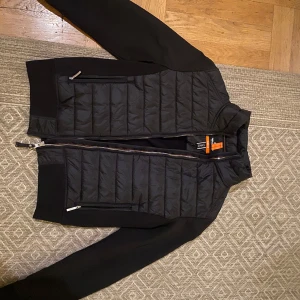 Svart jacka från Parajumpers junior stl - Snygg svart jacka från Parajumpers med quiltad design och dragkedja framtill. Jackan har långa ärmar och är tillverkad i fleece och syntetmaterial. Perfekt för kyligare dagar. Barn/ junior storlek se bild 