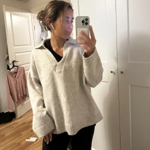 Grå stickad tröja från H&M - Mysig grå stickad tröja från H&M med en avslappnad passform. Tröjan har en krage och långa ärmar, perfekt för kyligare dagar. Enkel och stilren design som passar till det mesta.