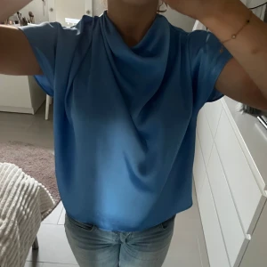 Blå blus med draperad hals - Snygg blå blus med draperad hals och korta ärmar. Perfekt för en stilren look. Blusen har en lös passform och är tillverkad i ett mjukt material som ger ett fint fall. Storlek S men passar XS-M skulle jag säga🤩perfekt till fest och passar både med jeans och kjol.