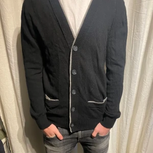 Cardigan tröja - Snygg svart kofta med knappar och kontrasterande detaljer vid fickorna. Perfekt för lager-på-lager och passar till många olika stilar. Tröjan är i bra skick och nypris ligger runt 1500-2000kr.