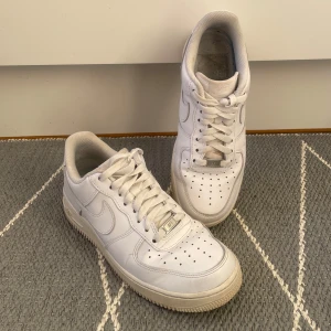 Vita Nike Air Force 1 sneakers - Säljer ett par klassiska vita Nike Air Force 1 sneakers. Skorna har en stilren design med snörning och perforerade detaljer på ovansidan för bättre ventilation. Perfekta för en avslappnad och trendig look. • Skorna är välanvända, men i gott skick utan några hål eller separationer. Motsvarar bilderna väl.