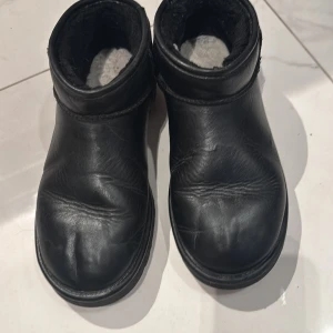 Svarta boots från UGG - Säljer ett par svarta boots från UGG i skinn med mjukt foder. Perfekta för kyliga dagar med sin robusta sula och bekväma passform. Enkla att ta på och av med dragflik baktill.
