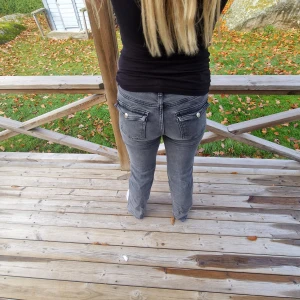 Grå jeans med knappar - Snygga grå jeans med knappar på bakfickorna. De har en bootcut passform och jeansen har en lågmidjade. De är mycket använda och tvättade och jättelite slitna längst ner och därav priset, men förutom det inga defekter. Dessa är i short length och passar min kompis på bilen som är ca 164, men även mig som är 161
