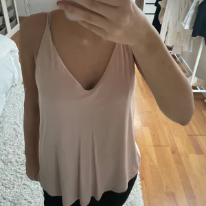 Rosa linnetopp - Säljer en stilren rosa linnetopp med smala axelband och v-ringning. Perfekt för varma dagar eller som ett lager under en kavaj. Toppen har en lös passform som ger en avslappnad look.