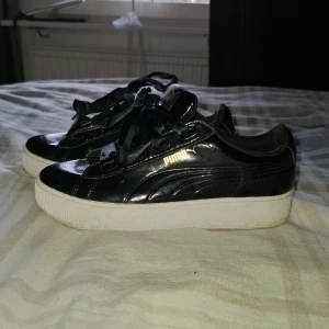 Svarta sneakers från Puma - Snygga svarta sneakers från Puma med glansig yta och breda snören. Skorna har en vit sula och Puma-loggan i guld på sidan. Skorna är andvända 1 gång. Nypris 913kr 