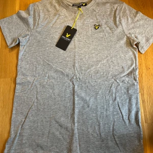 Grå t-shirt från Lyle & Scott - Snygg grå t-shirt från Lyle & Scott med korta ärmar och ett stilrent broderat emblem på bröstet. Perfekt för en avslappnad stil.