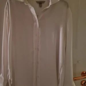 Vit långärmad skjorta från H&M - Säljer en stilren vit långärmad skjorta från H&M i storlek S/M Skjortan är tillverkad i 100% polyester och har en klassisk design med knappar framtill. Perfekt för en elegant och tidlös look.