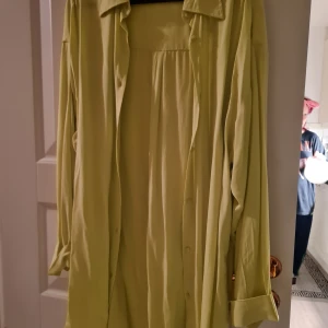 Ljusgrön skjorta från Kappahl - Säljer en ljusgrön klänning från Kappahl med långa ärmar och knappar framtill. Perfekt för en stilren och bekväm look.