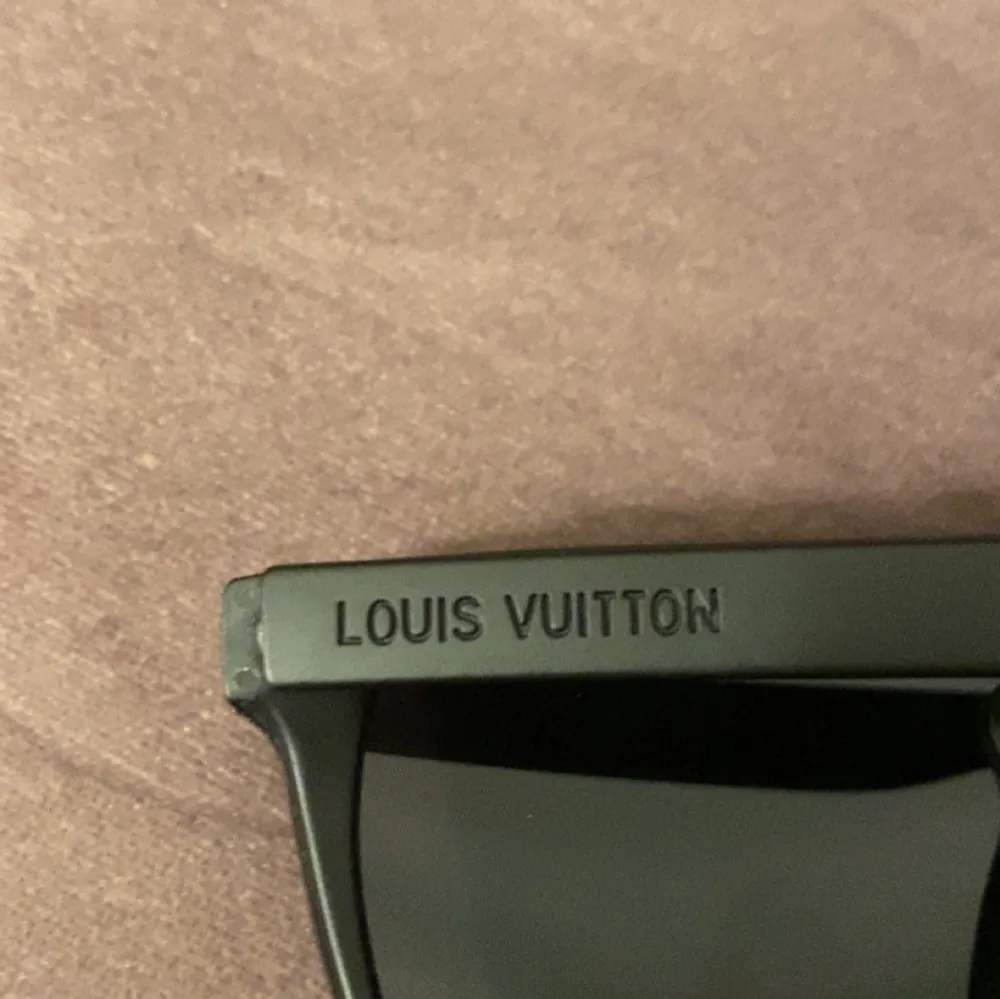 Stilrena svarta solglasögon från Louis Vuitton med monogrammönster på glasen. Tillverkade i Italien, dessa glasögon har en modern och edgy design med en bred ram och subtila detaljer. Perfekta för att ge en lyxig touch till din stil. OBS kan ej garantera att dom är helt äkta!. Muu.
