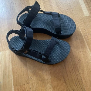Svarta Teva sandaler med justerbara remmar - Snygga och bekväma svarta sandaler med justerbara remmar för perfekt passform. Perfekta för sommardagar och strandpromenader.