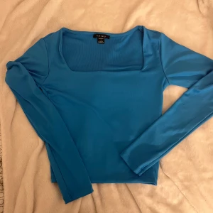 Blå topp - Fin blå topp som är lite croppad, långa ärmar. Använd en gång, har en liten fläck men kanske försvinner i tvätten. 