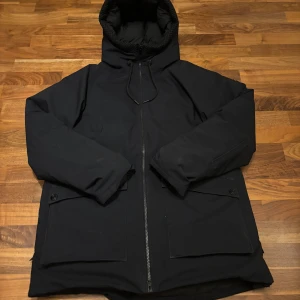 Svart vinterjacka med luva  - Säljer en varm peak performance jacka. Jackan är både vind- och vattentät, perfekt för kalla och blåsiga dagar. Den har långa ärmar och praktiska fickor framtill.