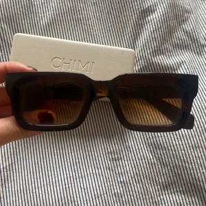 Bruna solglasögon från Chimi - Snygga bruna solglasögon från Chimi med en fyrkantig form. De har en robust design och kommer med ett stilrent fodral. Perfekta för att ge en cool touch till din look. Typ: 05 Brown.