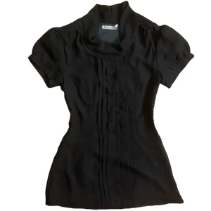 Svart polotopp från Mikarose y2k vintage  - Elegant svart/mörkgrå polotopp från Mikarose med korta ärmar och veckade detaljer framtill. Perfekt för en stilren look. Har zipper på sidan. Strl XS