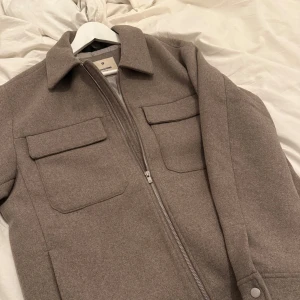 Beige jacka från Jack & Jones - Snygg beige jacka från Jack & Jones med dragkedja och två  bröstfickor. Med sin stilrena design och bekväma passform. Använd 1 gång och säljs pga att jag va snabb med att ta bort alla lappar så denna är helt ny i skicket, nypris: 1199kr. Hör av dig vid fler frågor!😇