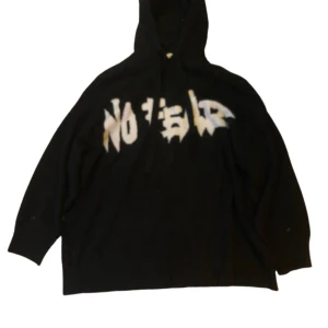 Svart hoodie med text - Cool svart hoodie med texten 'NO FEAR' i vit och beige på framsidan. Passformen är baggy, är nog en XL tror jag. Den är använd och har några fläckar men borde nog gå bort i en tvätt! Säljer fö jag inte använder den längre.