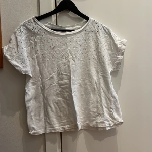 Vit topp från Jacqueline de Yong - Säljer en söt vit topp från Jacqueline de Yong i storlek M. Toppen har korta ärmar och ett fint broderat mönster framtill.