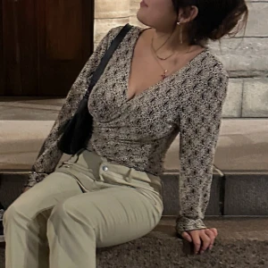 Svart och vit mönstrad omlottopp från Designwerket - Snygg svart och vit omlottopp från Designwerket med ett unikt mönster. Toppen är croppad och har långa ärmar samt en knytning. Perfekt för att ge en stilfull touch till din outfit.