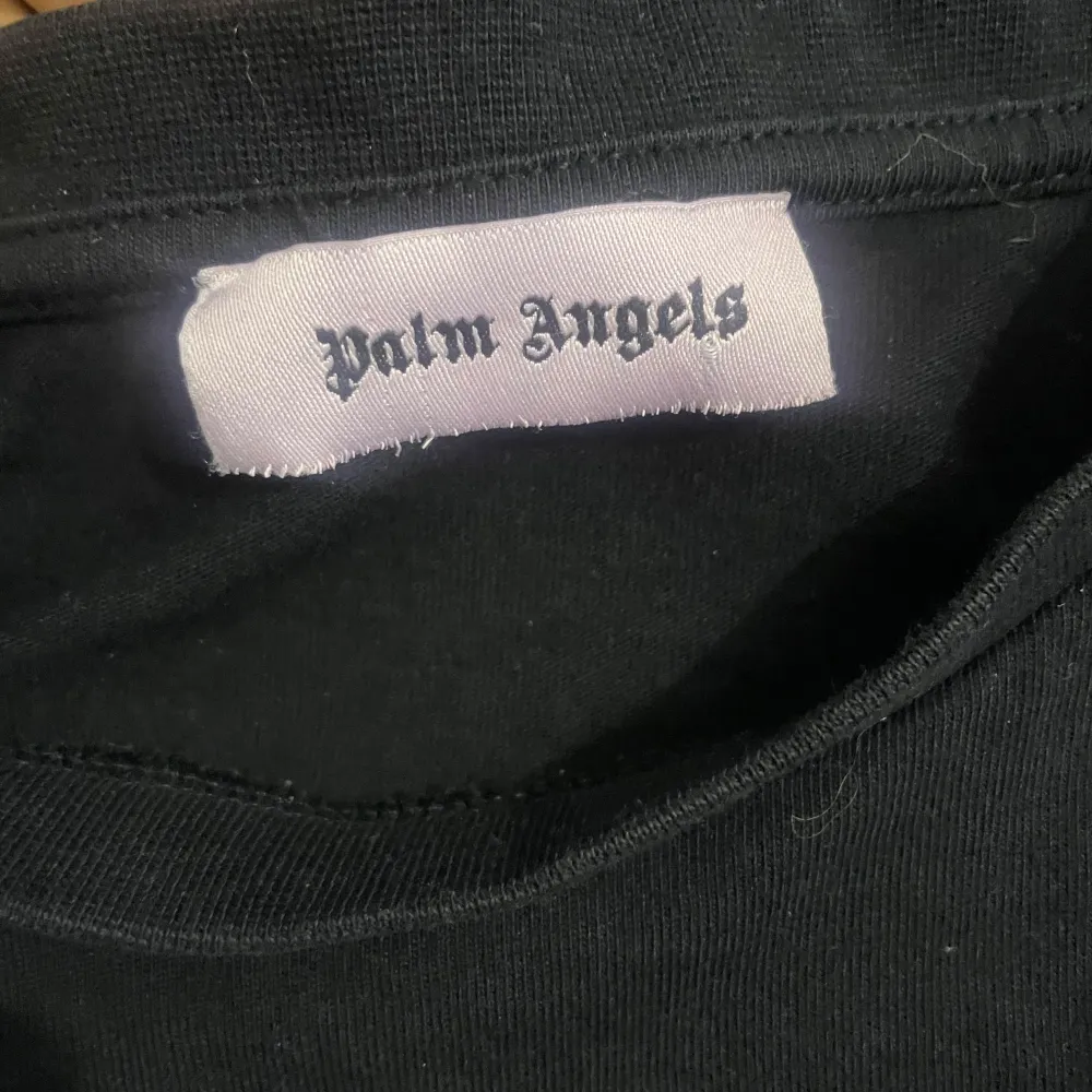 Säljer en svart t-shirt från Palm Angels med ett coolt tryck på framsidan där det står 'Palm Angels Milano' i vitt och gult. T-shirten är i bomull och har en normal    passform. Perfekt för en avslappnad stil den är oxå helt äkta  Pris går diskutera. T-shirts.