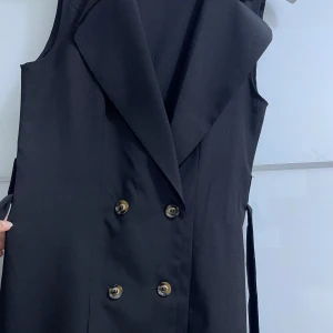  Skjort väst - En svart skjort väst med 4 knappar där fram och ett bälte till. Den är i ett nytt skick har använt den 1 gång. 