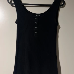 Svart ribbad linnetopp från Pieces - Säljer en snygg svart ribbad linnetopp från Pieces. Den har en enkel design med knappar framtill och är perfekt för både vardag och fest. Toppen är i storlek M och sitter skönt på kroppen.