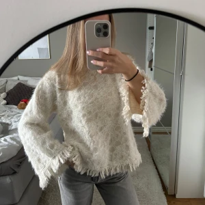 Vit tröja med fransar från Zara - Säljer en unik vit tröja från Zara med fransiga detaljer och ett cirkulärt mönster. Tröjan har långa ärmar och en lös passform, perfekt för en stilren look. Aldrig använd med prislapp kvar!