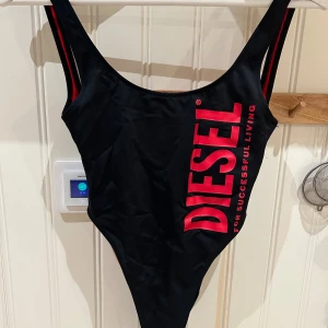 Svart baddräkt från Diesel - Snygg svart baddräkt från Diesel med röd logotyp på framsidan. Den har en djup rygg och breda axelband. 