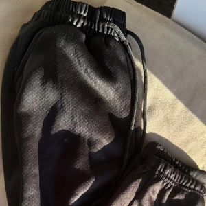 Svarta fleecefodrade mjukisbyxor - Mysiga svarta mjukisbyxor med fleecefoder för extra värme. Perfekta för kalla dagar när du vill hålla dig varm och bekväm. Byxorna har en elastisk midja med dragsko för justerbar passform.