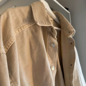 Beige overshirt med knappar - Snygg beige overshirt med knappar och en bröstficka. Perfekt för lager-på-lager-stil. Den har en klassisk krage och långa ärmar, vilket gör den idealisk för både vår och höst.