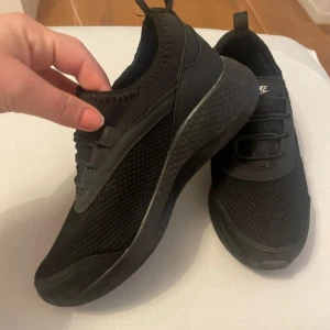 Svarta Nike sneakers - Snygga svarta Nike sneakers med en stilren design. Skorna har en bekväm passform och är tillverkade i syntetmaterial med snörning. Perfekta för vardagsbruk och träning.