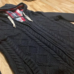 Mörkblå stickad tröja med dragkedja - Säljer en marinblå stickad hoodie med dragkedja och rutigt foder i huvan. Tröjan har ett snyggt flätmönster och väldigt snygga detaljer! Vet inte vilket märke det är men materialet är väldigt skönt och varmt. Sitter som S/M