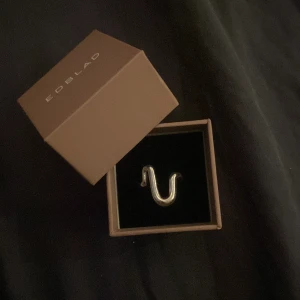Silverfärgad ring från Edblad - Snygg och modern silverfärgad ring från Edblad med en unik, böjd design. Perfekt för att ge en stilren touch till din outfit. Kommer i originalförpackning.