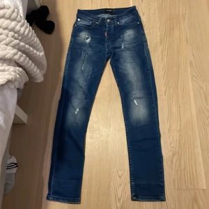 Blå jeans från Dsquared2 - Snygga blå jeans från Dsquared2 med slitna detaljer och en klassisk femficksdesign. Jeansen har en knappgylf och en liten röd etikett med logotypen. Perfekta för en trendig look.