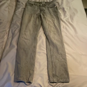 Grå jeans med slitna detaljer - Säljer ett par grå jeans med slitna detaljer vid bensluten. De har en klassisk femficksdesign och en rak passform. Perfekta för en avslappnad stil. Low waist.