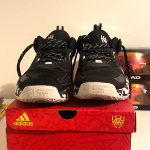 Svarta Adidas basketskor med mönstrad sula - Snygga svarta Adidas sneakers med vit och svart mönstrad sula. Skorna har snörning och är designade i samarbete med Donovan Mitchell. Perfekta för en sportig look.