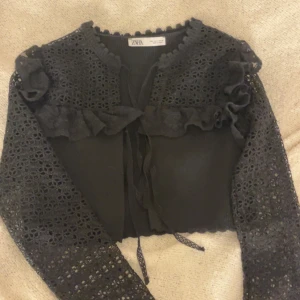 Svart spetskofta från Zara - Elegant svart kofta från Zara med vackra spetsdetaljer och volanger. Den har långa ärmar och knytband framtill. Storlek M men är som en S Tryck inte köp nu! Kontakta mig om du vill köpa eller är intresserad❤️