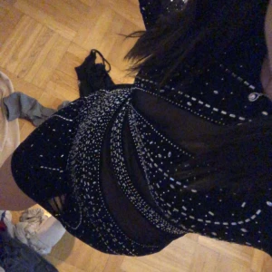 Svart glittrig klänning  - Snygg svart klänning med glittriga detaljer och meshpartier. Den har en tight passform och långa ärmar, perfekt för en kväll ute. Klänningen är kort och har ett unikt mönster som verkligen sticker ut. Använd en gång under nyår. 